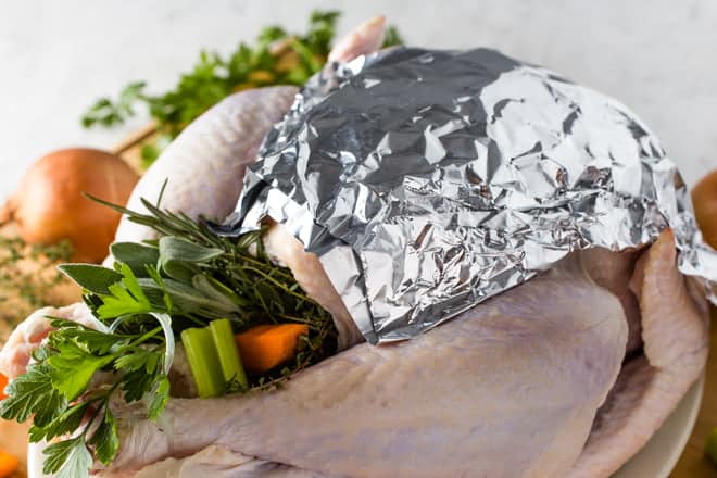 Raw stuffed turkey with foil over breasts.