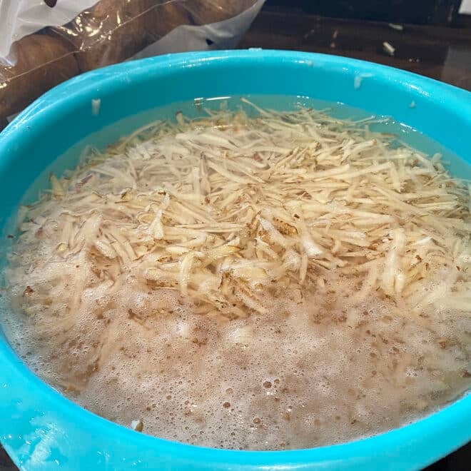 A big bowl of shredded potatoes soaking in cold tap water