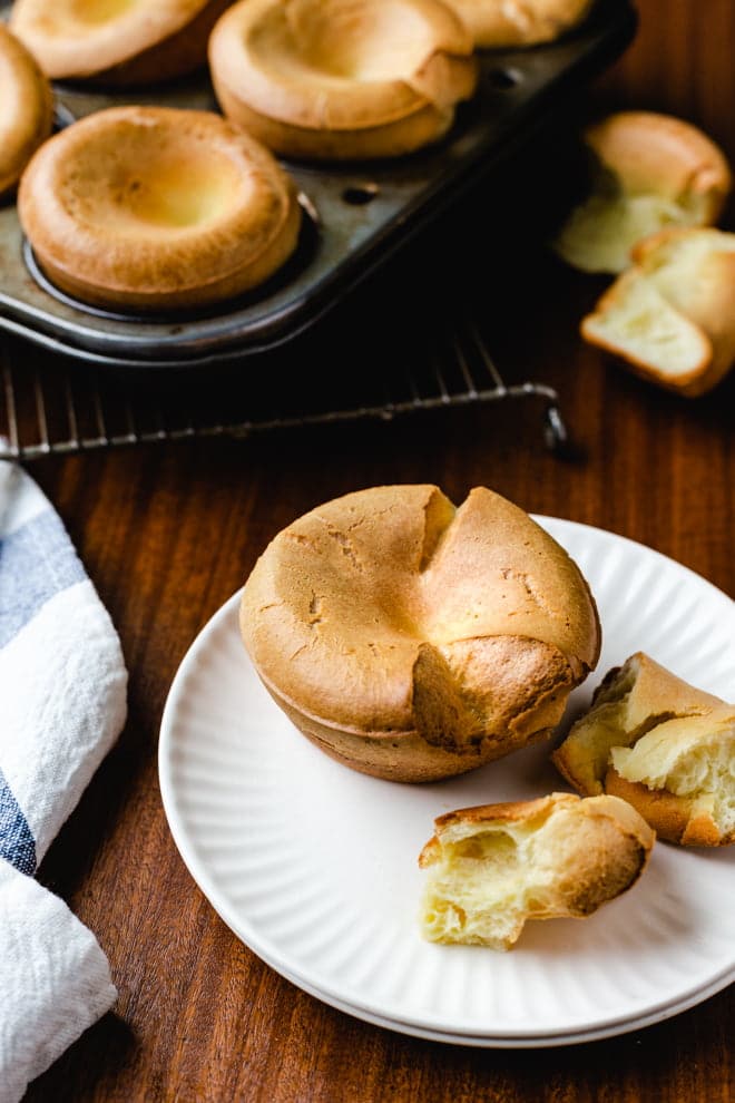Popover on a white plate with muffin tin in background.