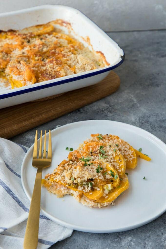 Butternut squash gratin on a white plate with a fork, casserole dish in background.