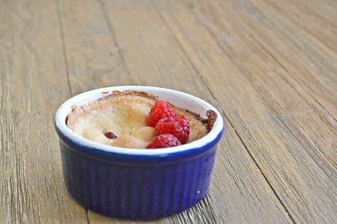 Mini pie in a blue ramekin with fresh raspberries on top.