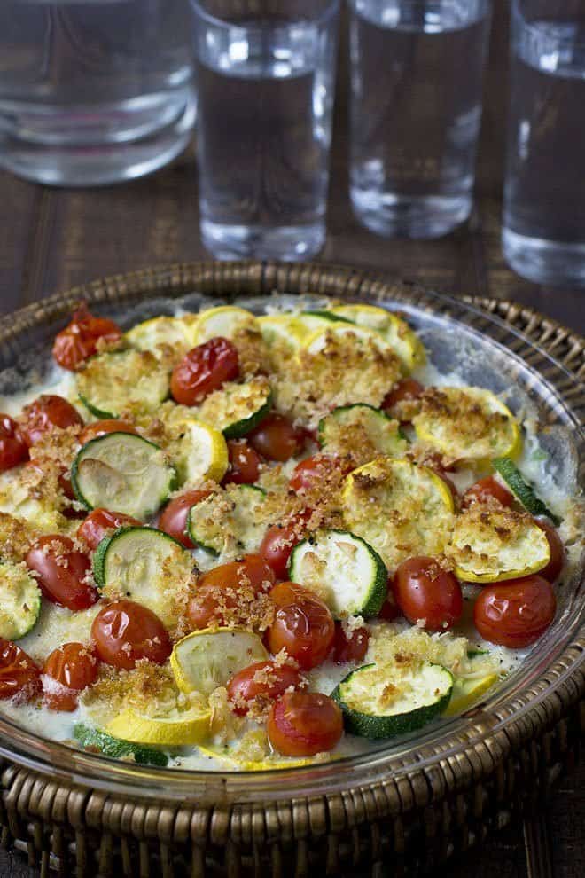Glass dish with zucchini, yellow squash, and tomato gratin with breadcrumbs on top.