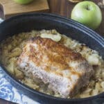 Pork and Sauerkraut in a roasting dish with apples and onions in background.