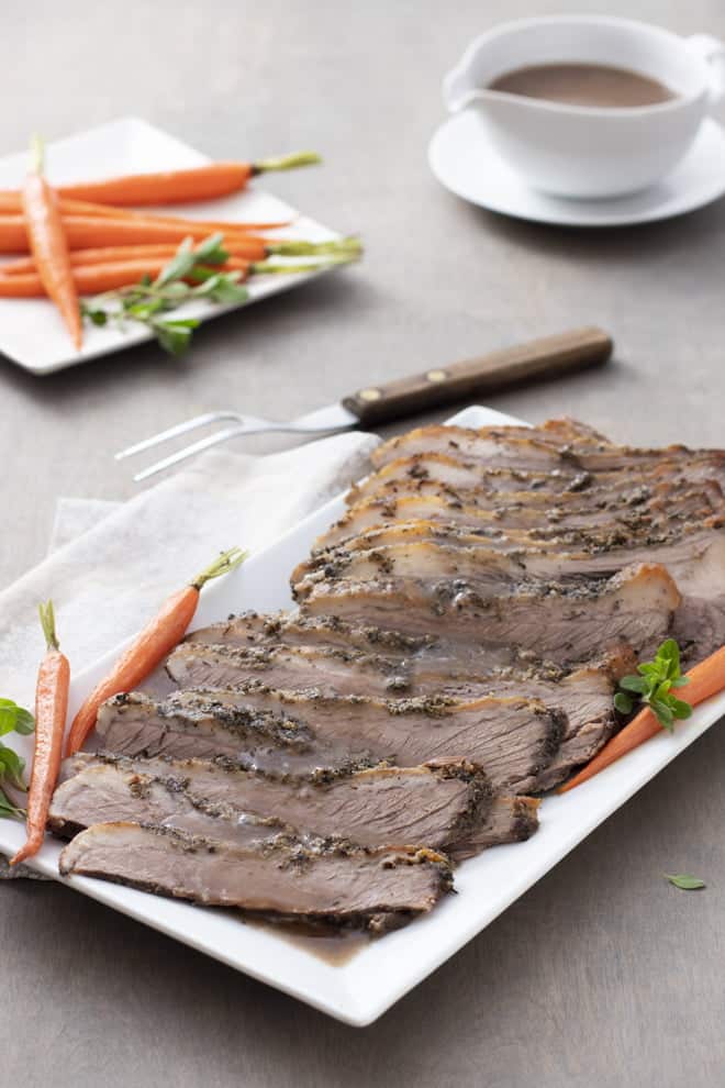 Sliced beef brisket on a white platter with carrots.