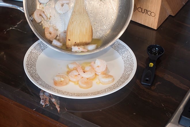 Pouring shrimp in buttery sauce onto a plate.