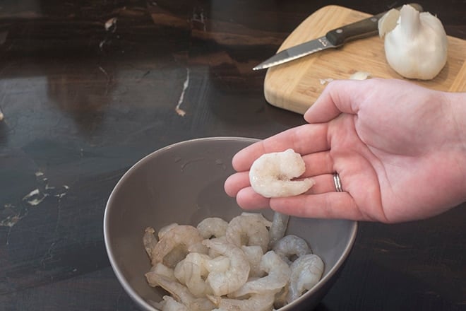 Thawed shrimp in a hand over a bowl of shrimp.