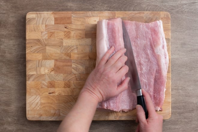 Cutting a raw pork loin on a cutting board.