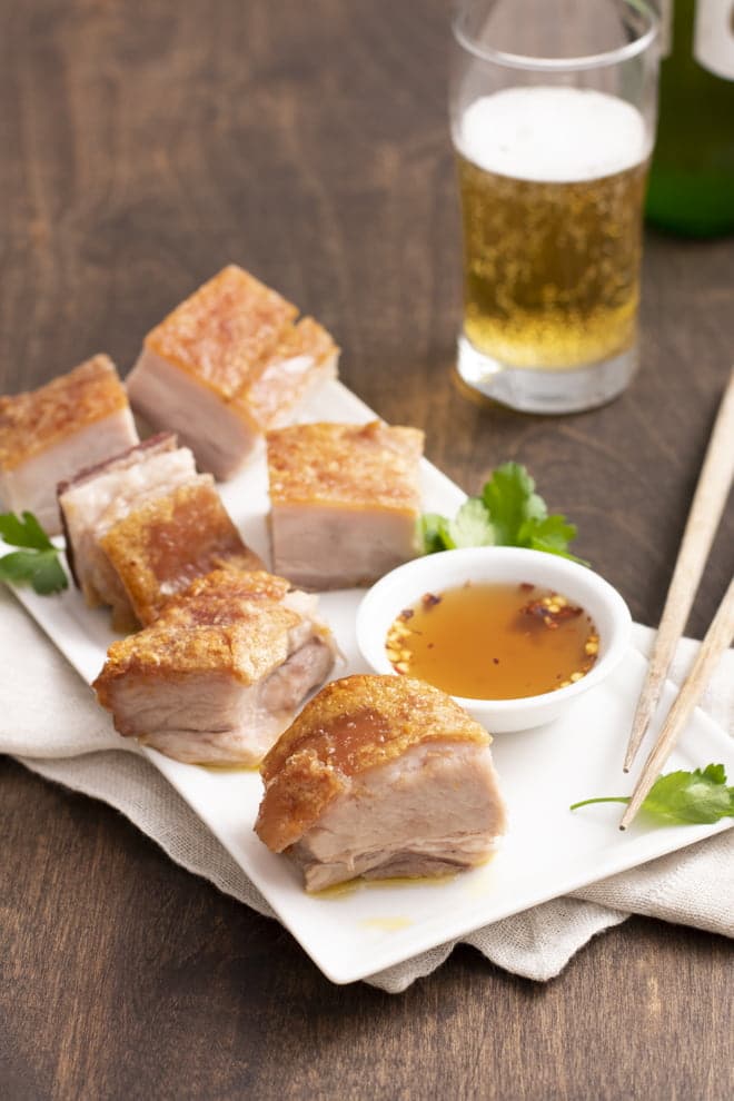 Pork belly on white plate with chili dipping sauce and chopsticks.