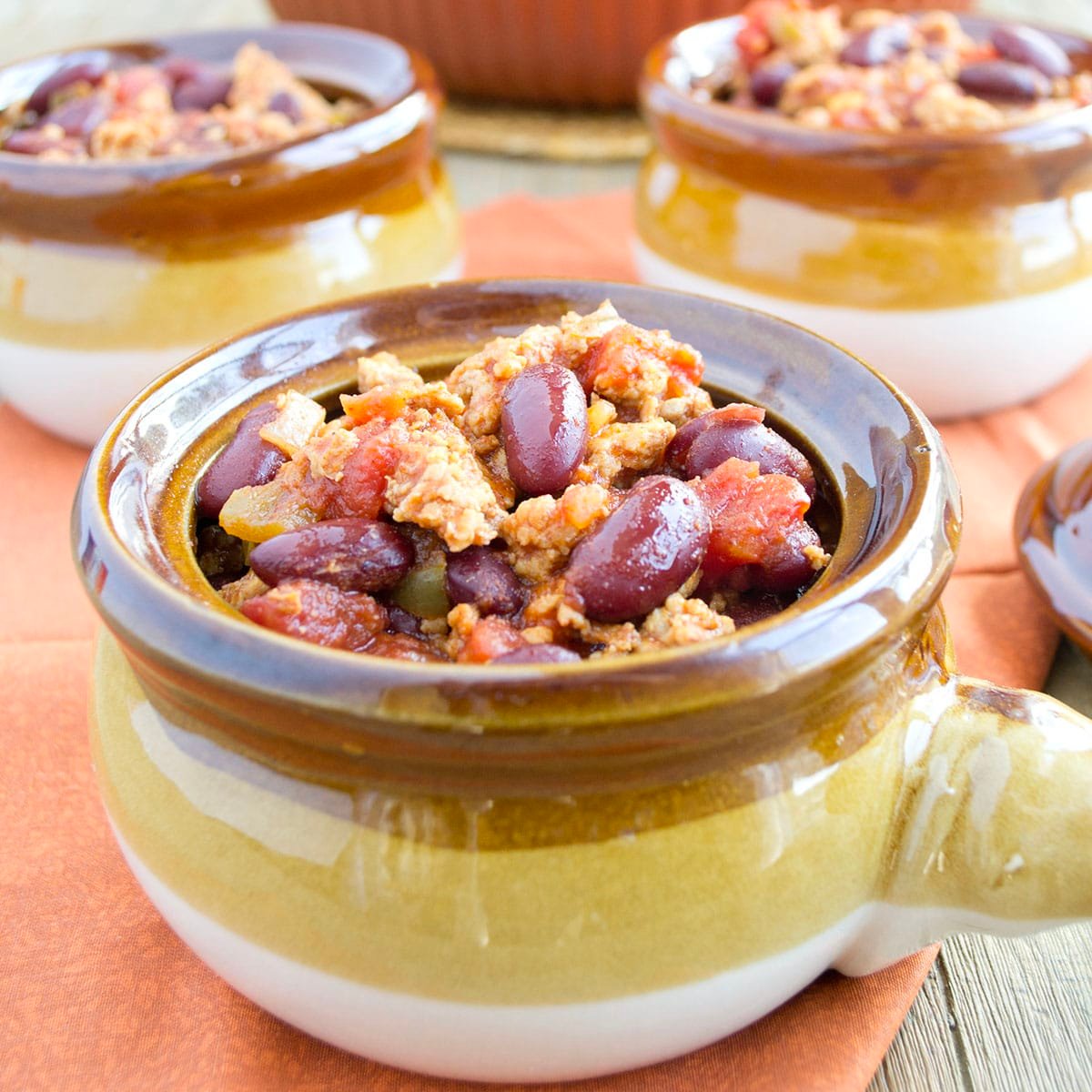 Ceramic bowl with a yellow and brown strip filled with chili with ground meat and beans.