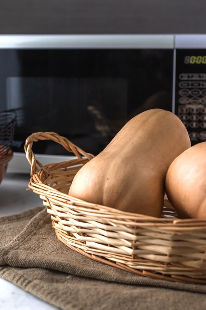 Butternut squashes in basket in front of microwave.