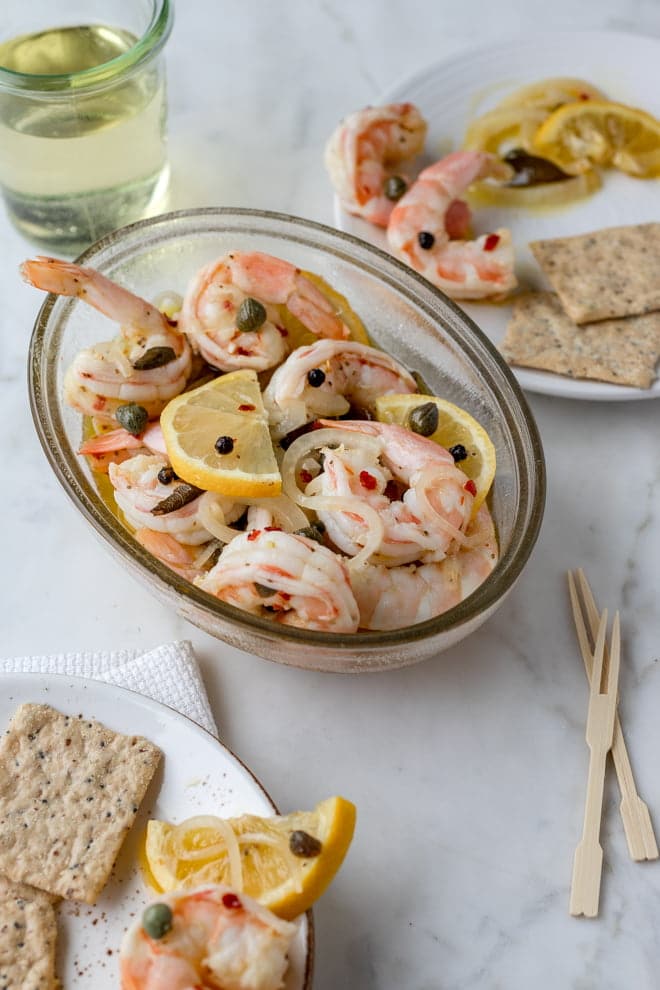 Pickled shrimp in a glass dish with lemon slices.