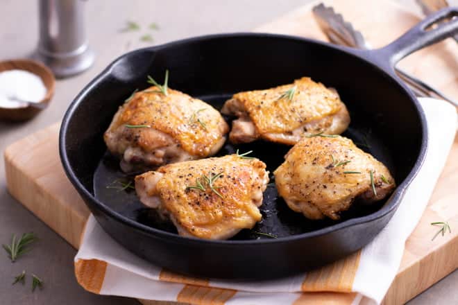 Skin-on chicken thighs in a cast iron pan.