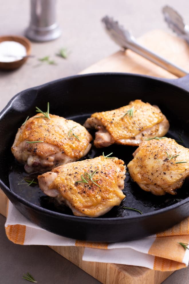 Skin on chicken thighs in a cast iron pan.