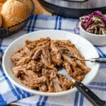 A pile of pulled pork in a bowl, an Instant Pot in the background