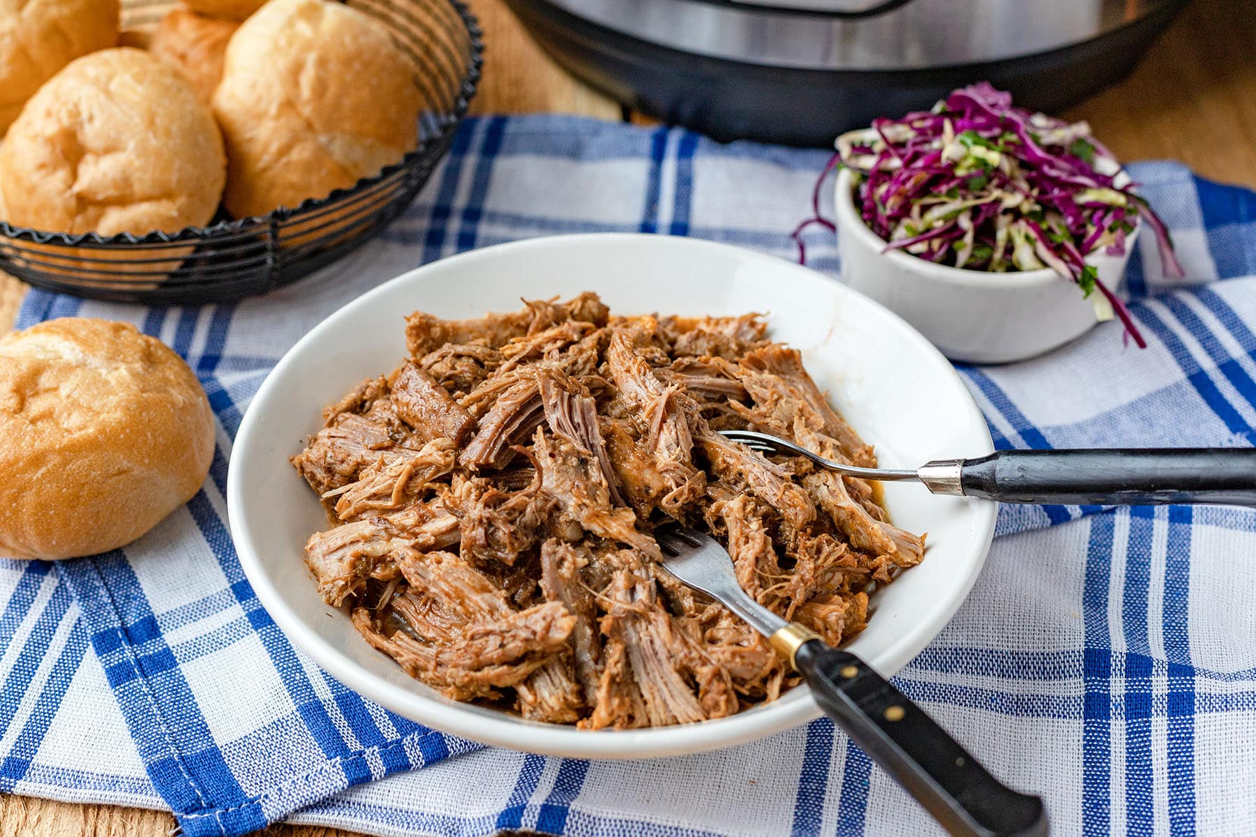 A pile of pulled pork in a bowl, an Instant Pot in the background