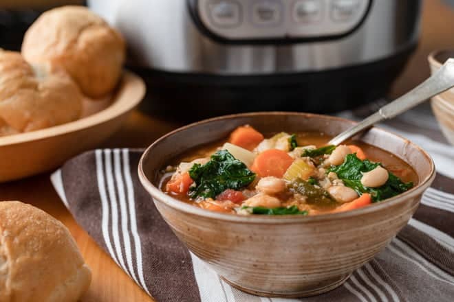 Vegetable Soup in a brown bowl in front of an Instant Pot, rolls off to the side.