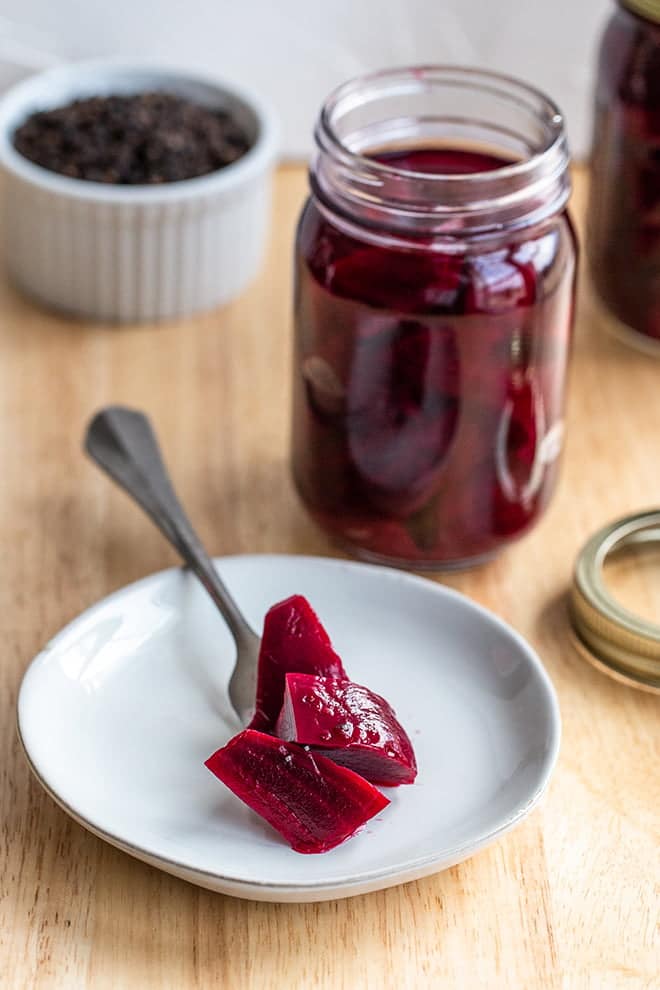 Pickled beets on a fork on a plate and in a glass jar.