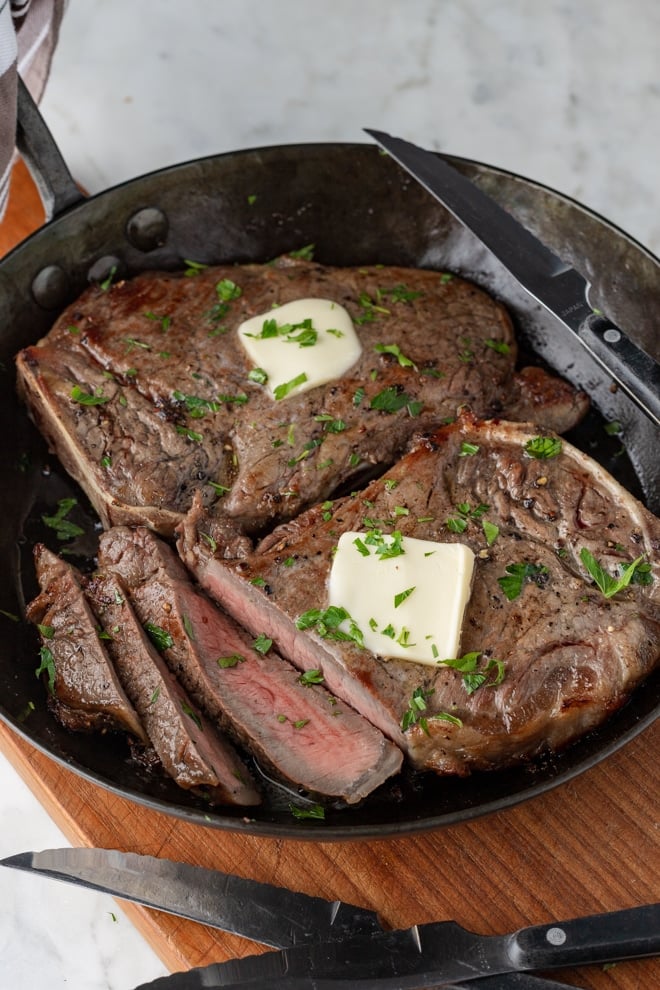Steak in a pan topped with butter and parsley.