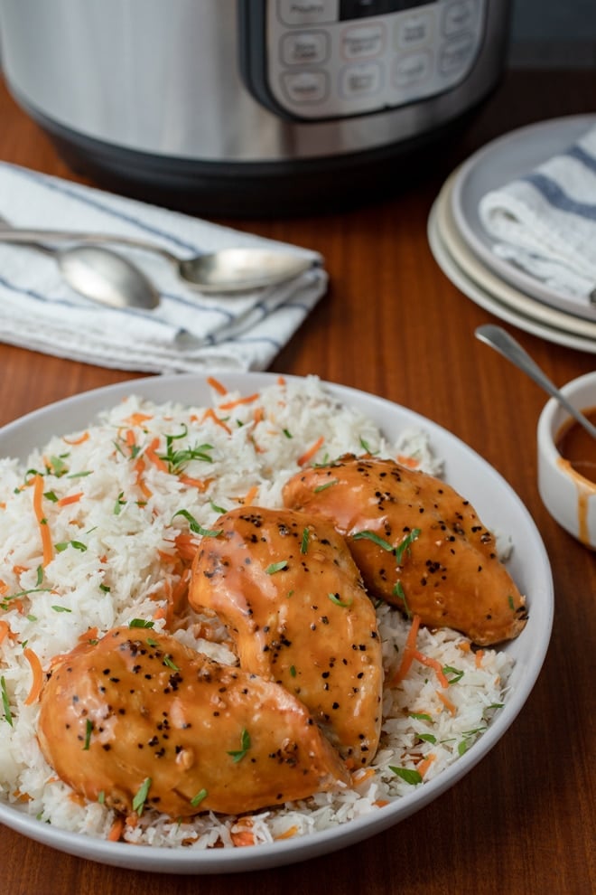 Chicken with an orange ginger glaze, and coconut rice studded with carrots on a white plate in front of an Instant Pot.