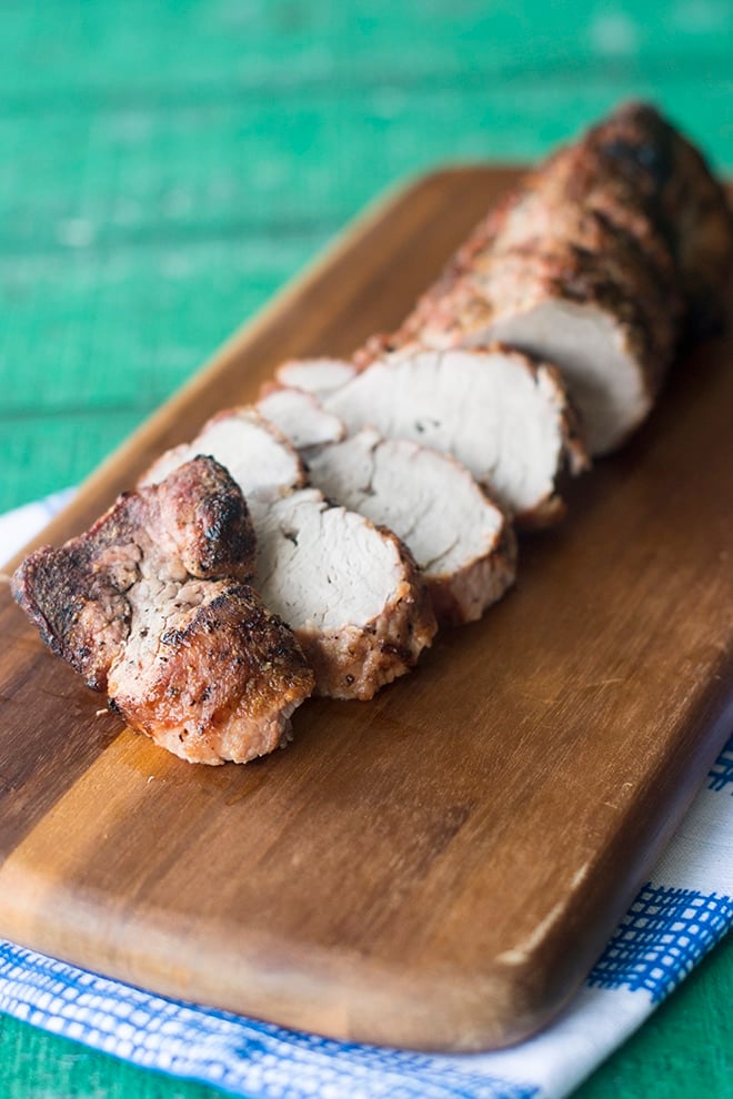 Pork tenderloin on a wooden cutting board, with several slices cut.