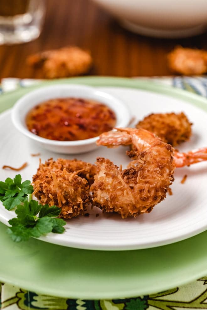 Crispy coconut shrimp on a white plate with dipping sauce.