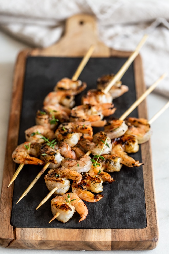 Wooden skewers of grilled shrimp on a wooden board.
