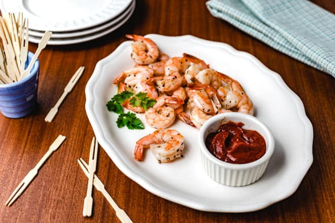 Roasted shrimp on a white platter with a dish of cocktail sauce.