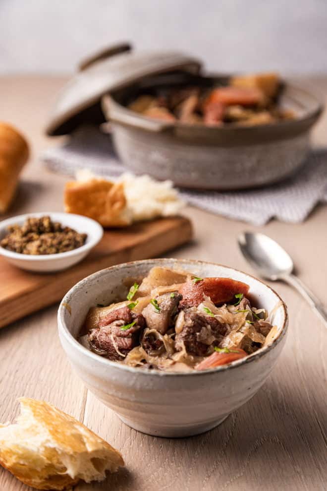 Polish hunter's stew with pork, sausage, and sauerkraut in a deep bowl, crusty bread to the side.