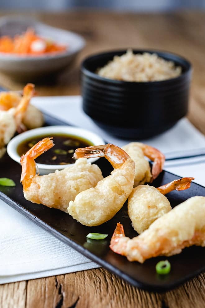 Shrimp Tempura on a black platter with a dipping sauce.