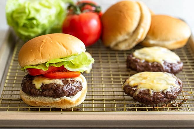 Burger patties with cheese on rack. Burger made with lettuce and tomato.