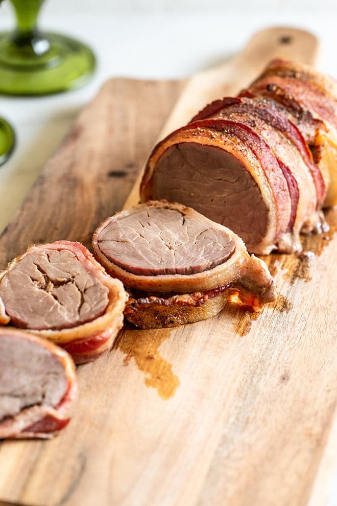 Bacon-Wrapped Pork Tenderloin on a wooden cutting board, with several slices cut.