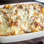 Baked ziti in a white casserole dish. Spatula lifting up a serving.