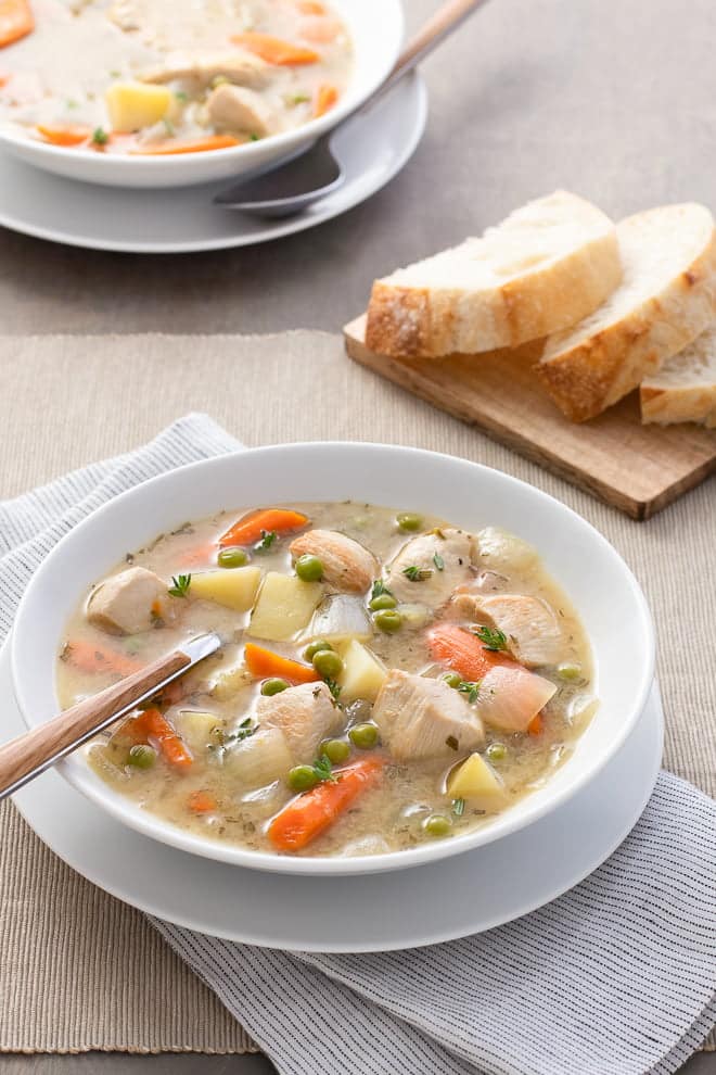 Chicken stew with carrots and peas in a white bowl.