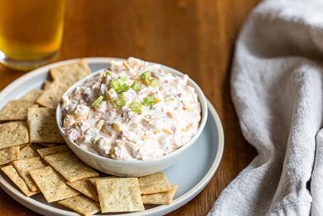 Creamy Corn Dip in a white bowl on a plate with crackers.