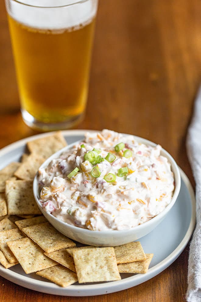 Creamy corn dip in a bowl sitting on a plate with crackers.
