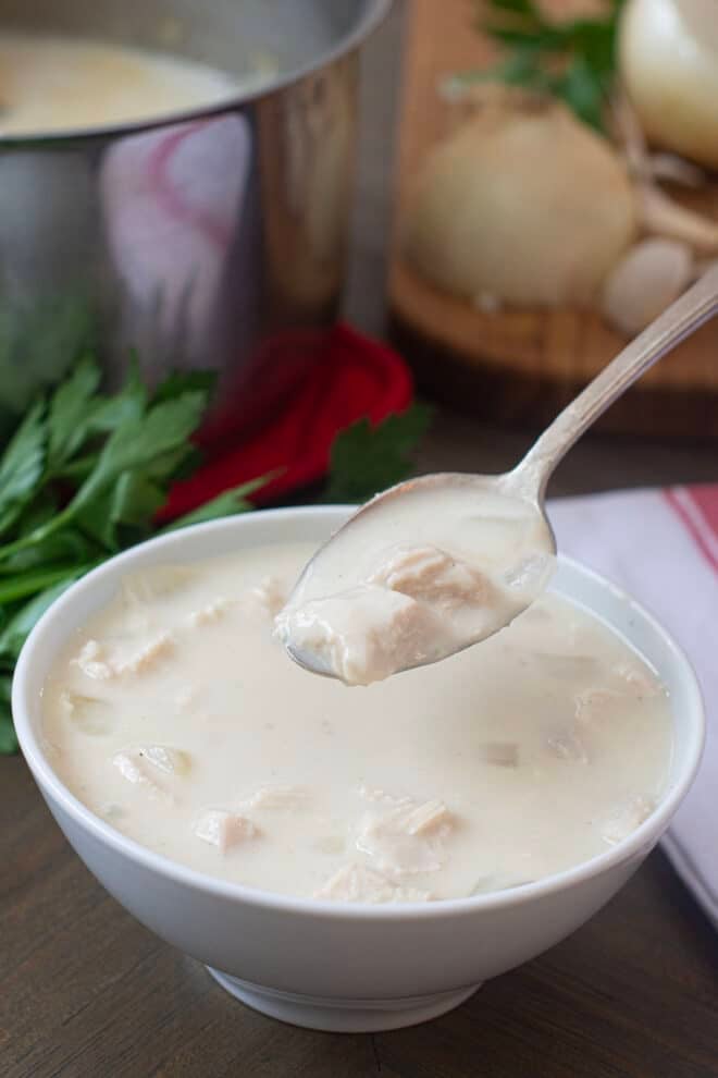 A bowl of cream of chicken soup with a spoonful of soup held above showing the pieces of chicken, pot of soup in the background