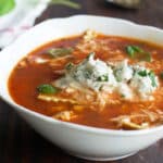 Lasagna Soup in a white soup bowl, topped with ricotta and basil.