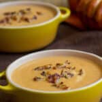Pumpkin soup with bacon crumbles in yellow bowls.