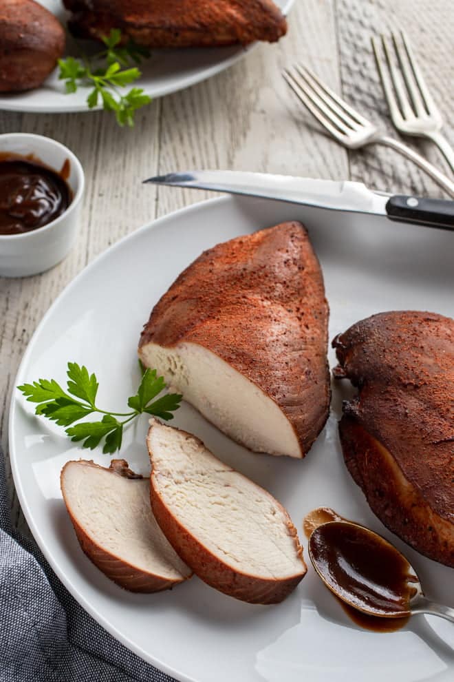 Smoked Chicken Breasts on a white plate with spoonful of BBQ sauce.