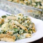 Spinach and Artichoke Pasta Bake on a white plate with baking dish in background.