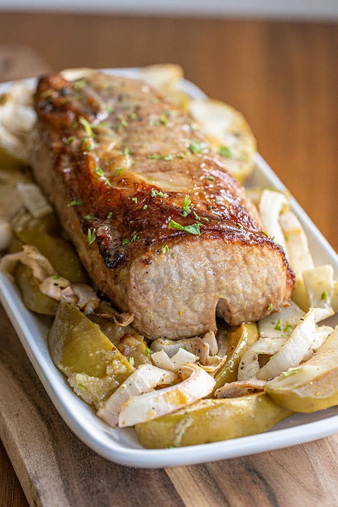 Juicy, glazed pork loin on a white platter with apples and onion.