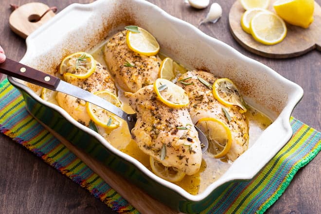 Chicken breasts with lemon slices in a white baking dish.