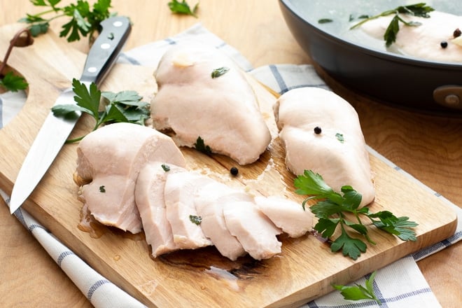 Cutting board with whole and sliced poached chicken breasts.