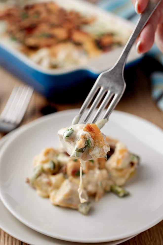 Forkful of Jalapeno Popper Chicken Casserole with plate and casserole dish in background.
