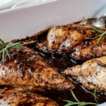 Chicken breasts in a balsamic sauce in a white baking dish.