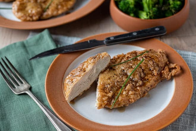 Crunchy honey garlic coated chicken breast with slice cut on a white and brown plate.