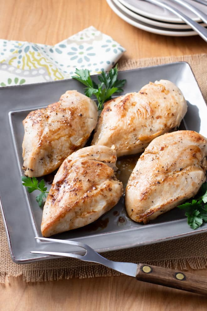 Four pan-fried chicken breasts on a gray platter.
