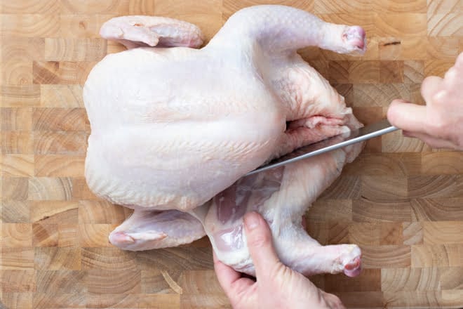 With the chicken laying on its back on a cutting board, make a cut into the skin where one of the thighs meets the body.