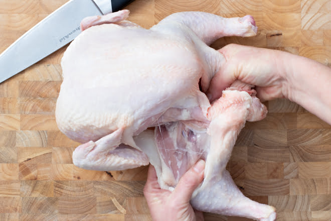 Folding leg quarter of raw chicken back to separate from body.