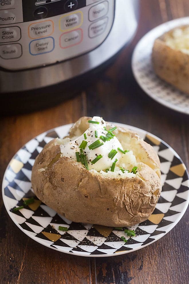 Baked potato topped with sour cream and chives, in front of an instant pot.